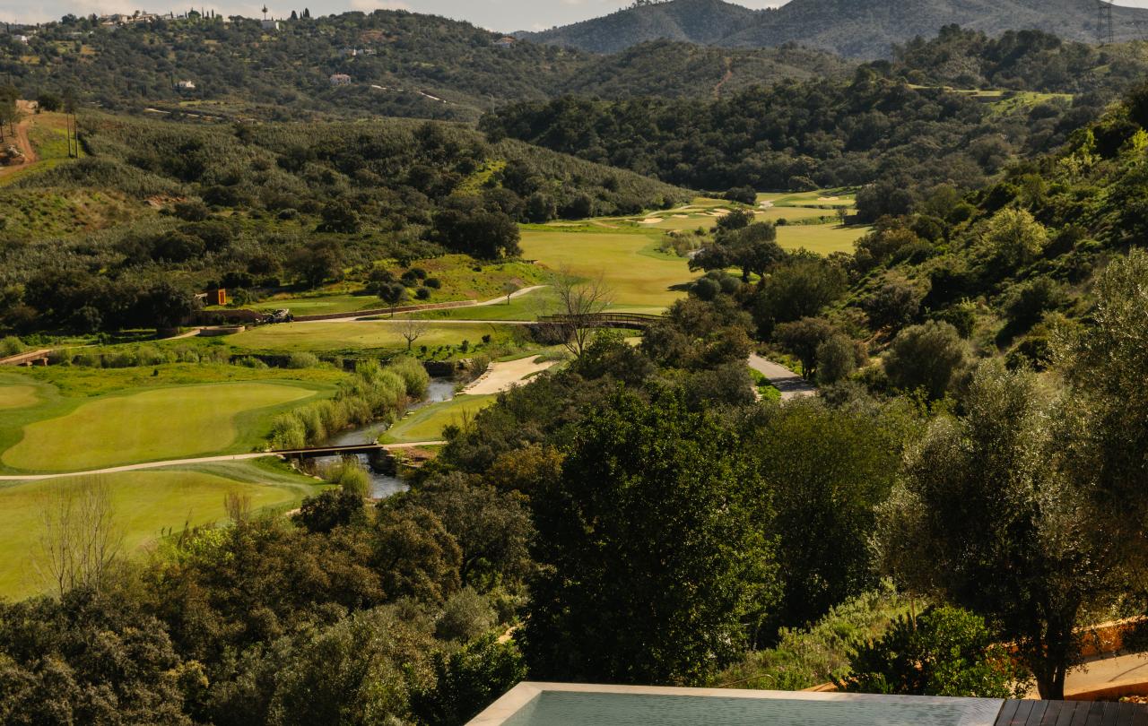 Vista aérea de uma piscina infinita de um resort com vista para um campo de golfe exuberante e colinas verdes.