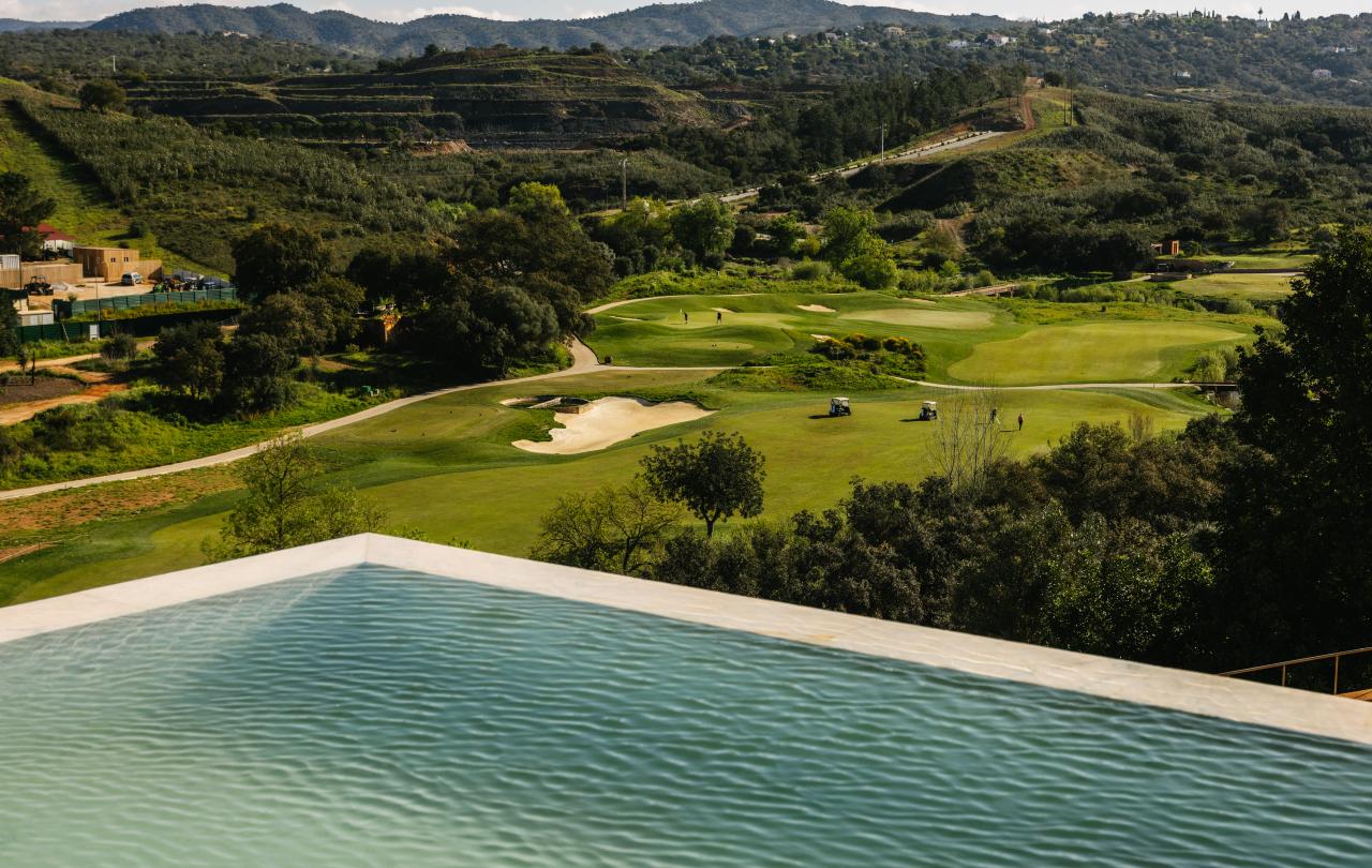 Grande plano das águas cristalinas da piscina infinita, que se estendem em direção a uma paisagem distante de um campo de golfe verdejante.