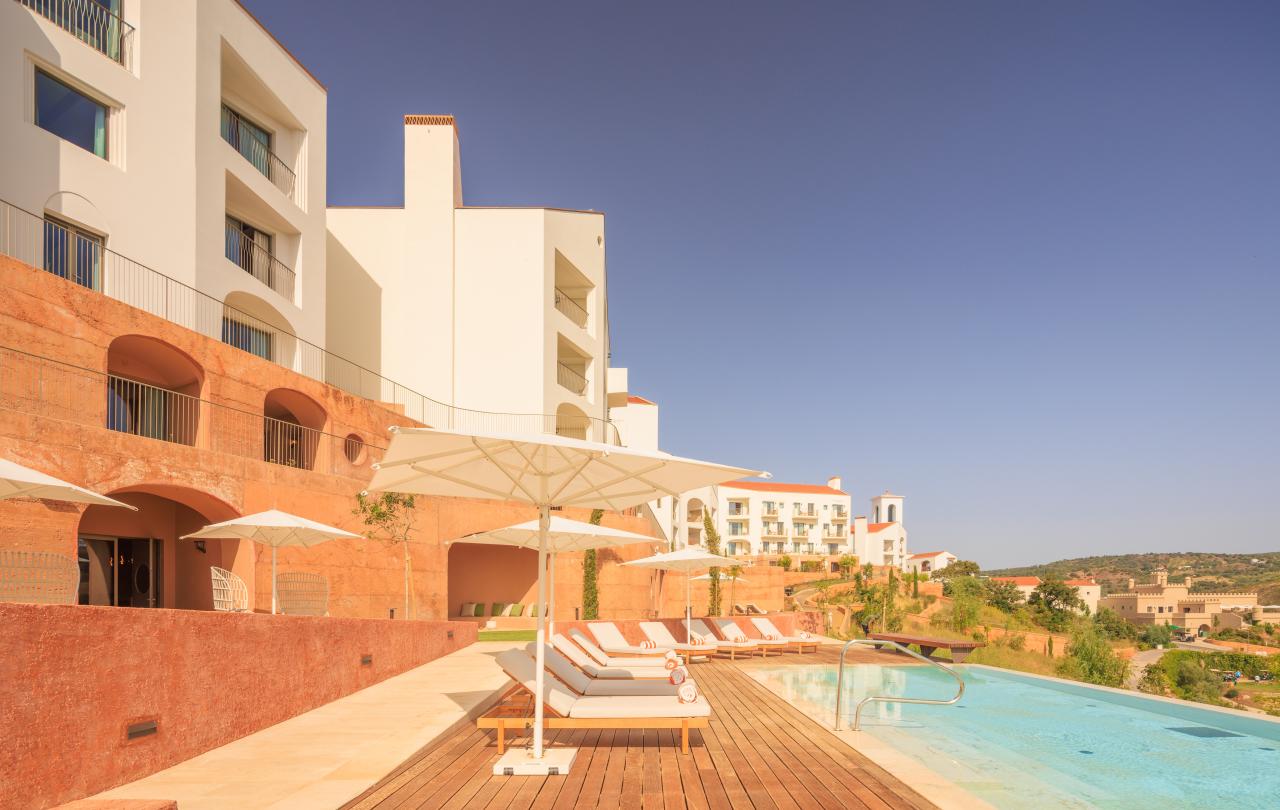 Hotel moderno com edifícios brancos e uma piscina infinita com vista para uma cidade situada numa encosta.