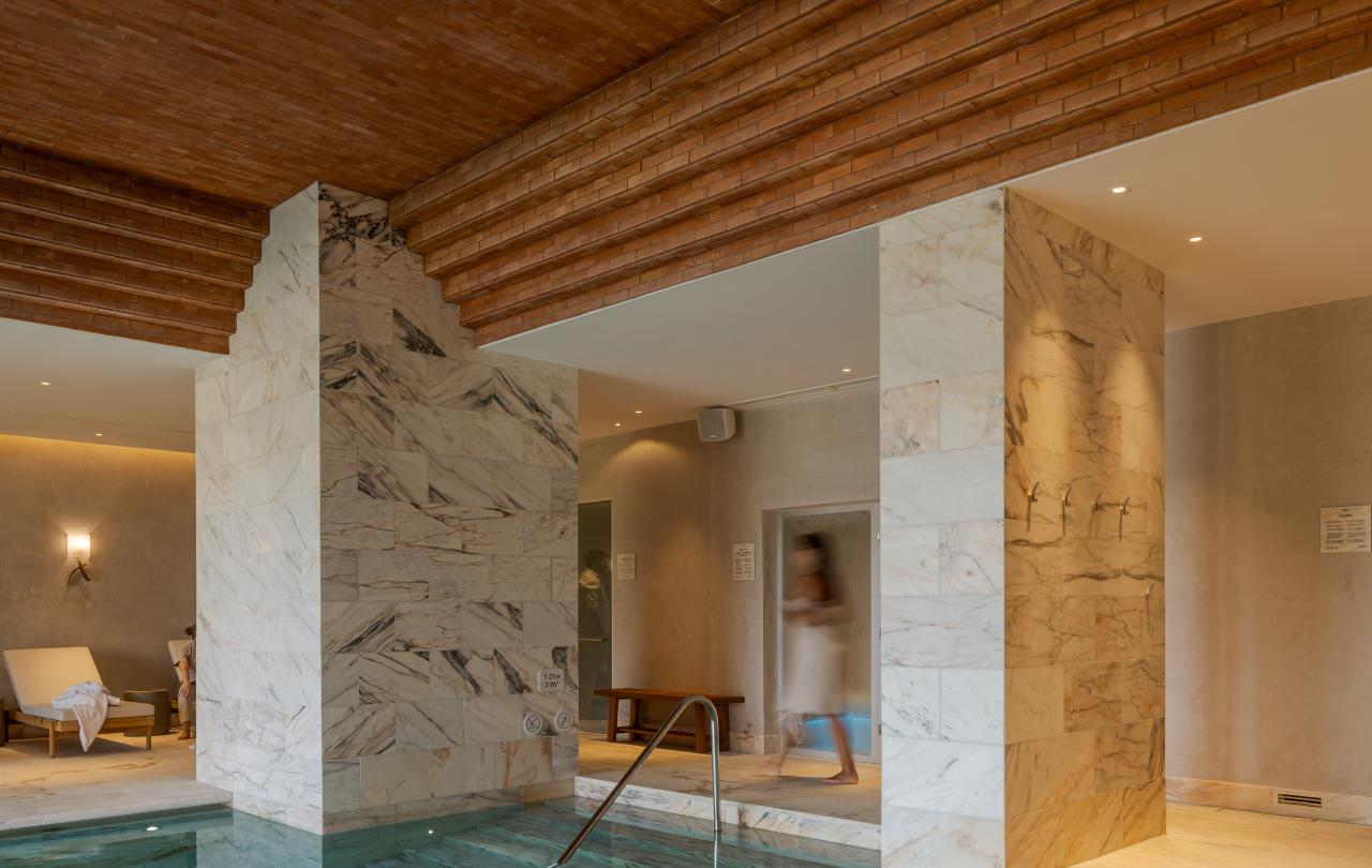 Uma piscina interior com pilares de mármore e um teto de madeira com textura, criando um ambiente luxuoso e sereno.