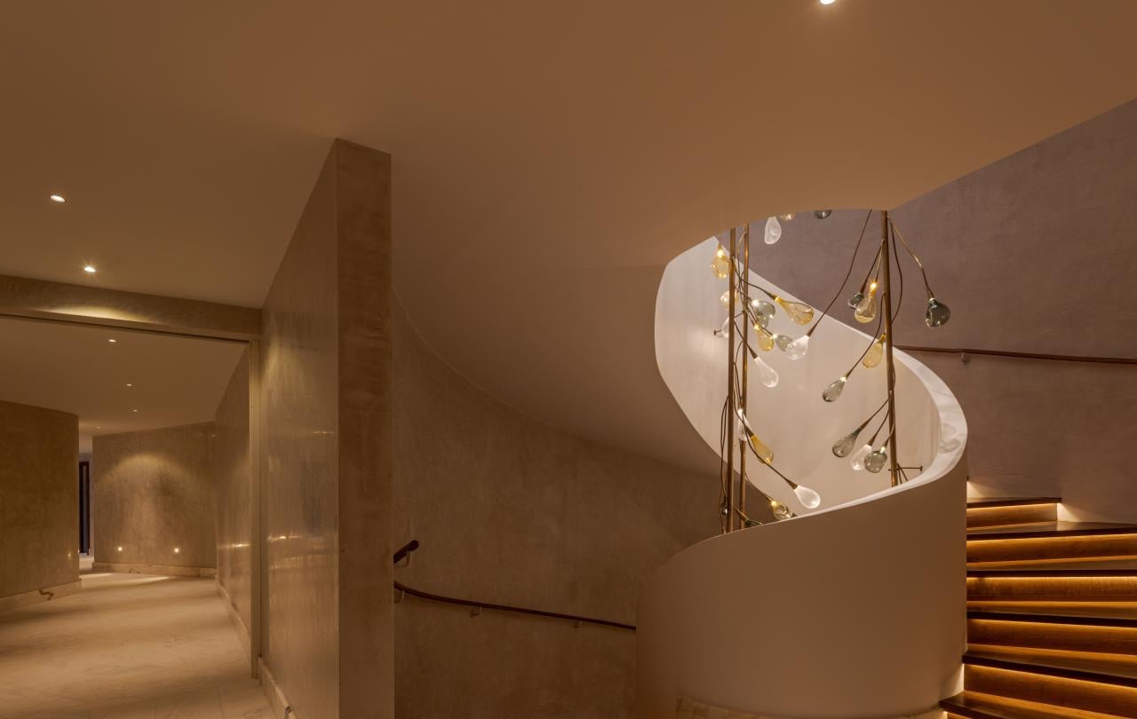 Interior com iluminação acolhedora, com uma escadaria em espiral moderna e um candeeiro suspenso artístico.