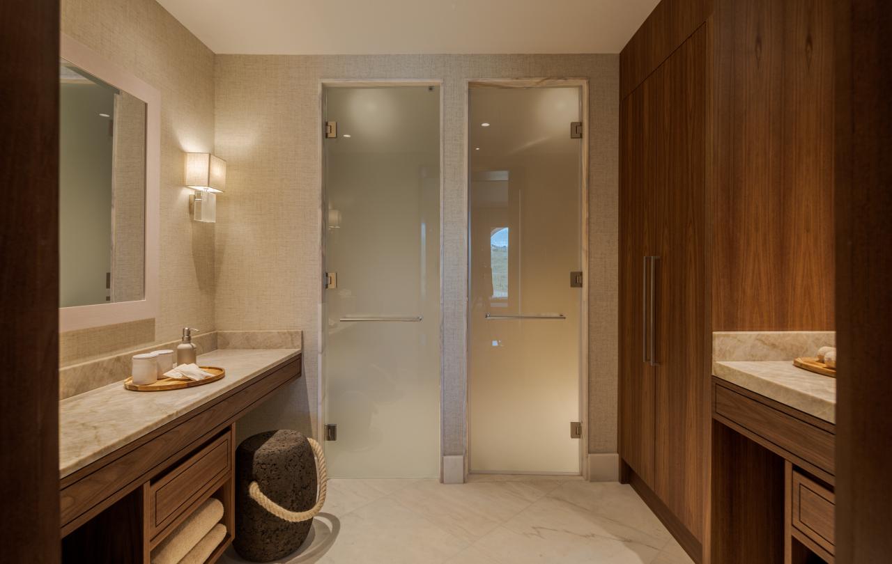 Vestiário de spa elegante com bancadas de maquilhagem, armários de madeira e portas de vidro fosco.
