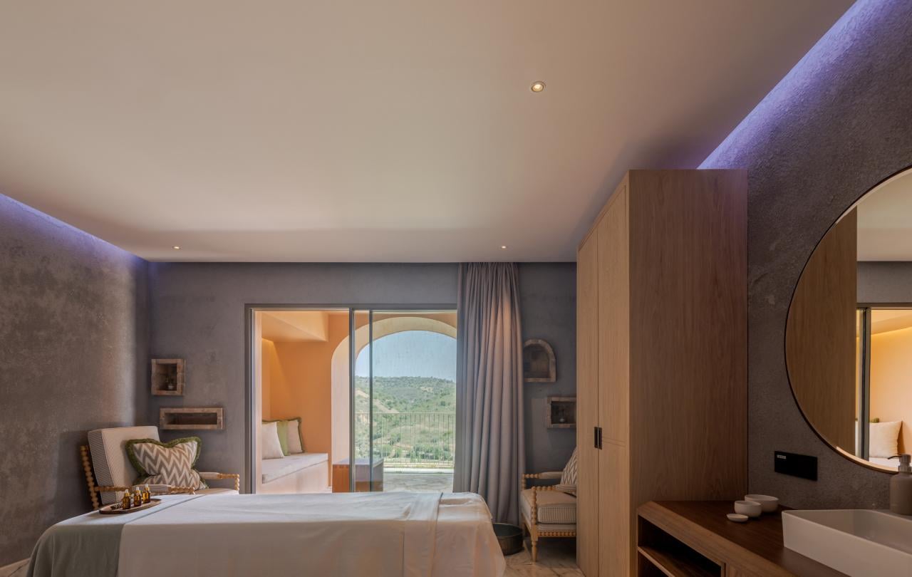 Sala de tratamentos de spa luxuosa, com duas marquesas de massagem, iluminação ambiente suave e vista para o terraço.