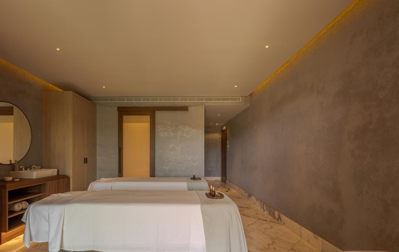 Sala de massagens espaçosa com duas marquesas preparadas para tratamentos, pavimento em mármore e iluminação ambiente acolhedora.