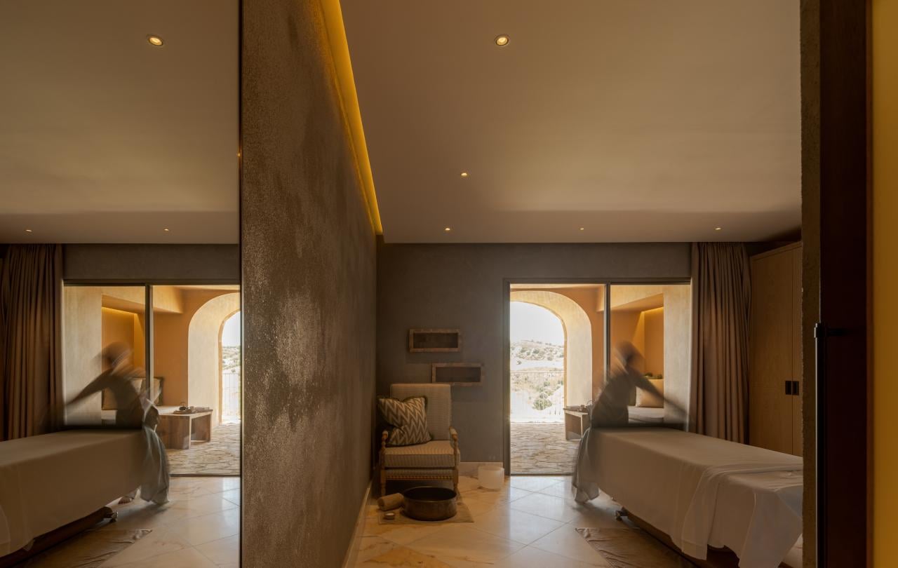 Vista simétrica de uma sala de spa serena, com uma marquesa de massagem refletida num espelho de corpo inteiro.
