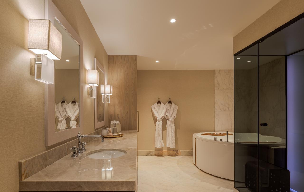 Casa de banho luxuosa com um lavatório comprido em mármore, roupões de banho brancos e macios e uma banheira circular.
