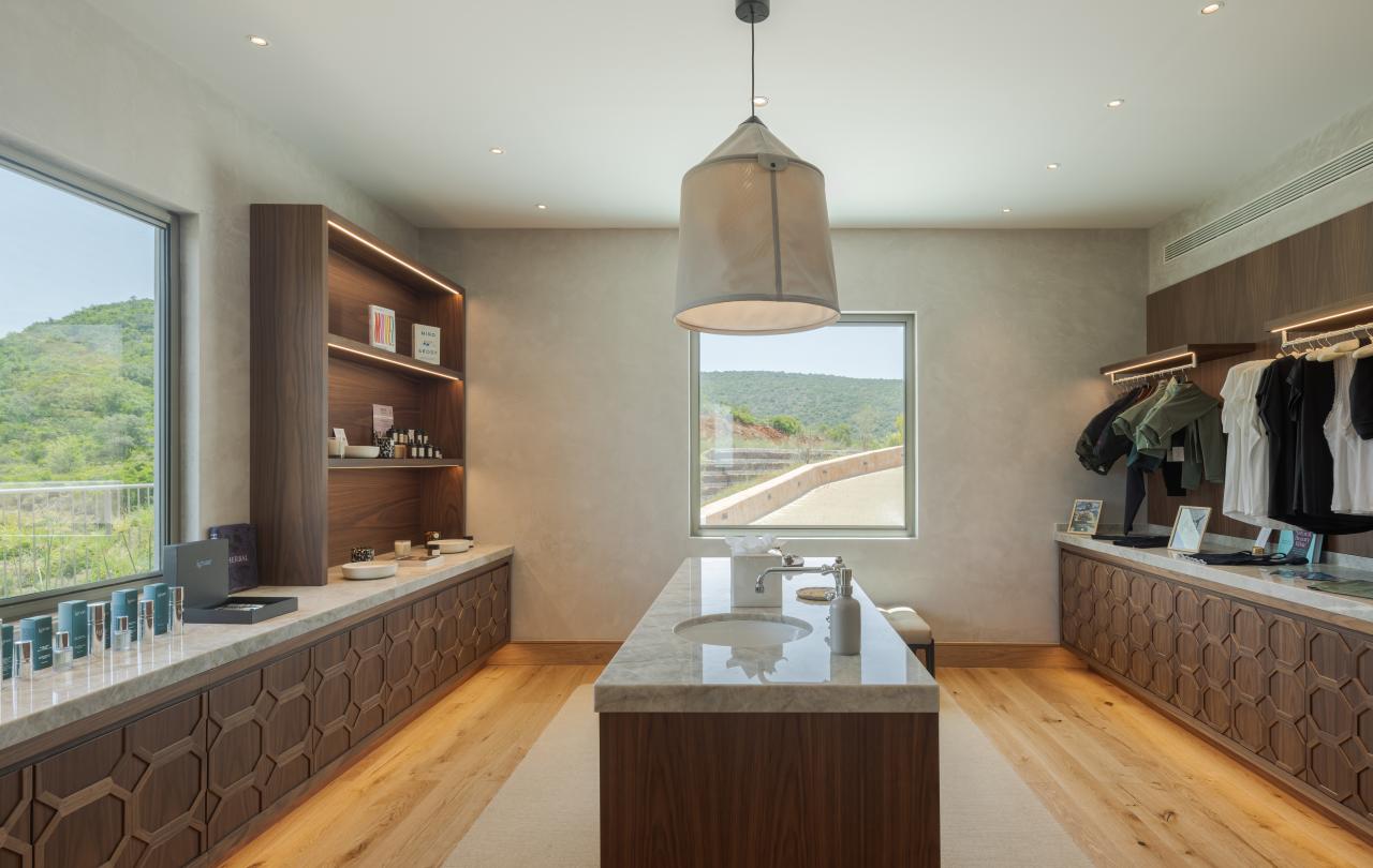 Showroom de retalho que exibe produtos de spa e peças de vestuário penduradas em torno de uma ilha central com tampo de mármore.