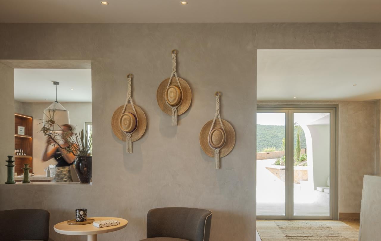 Recanto de estar com duas poltronas cinza-escuro, uma mesinha e chapéus de palha em macramé decorativos na parede.