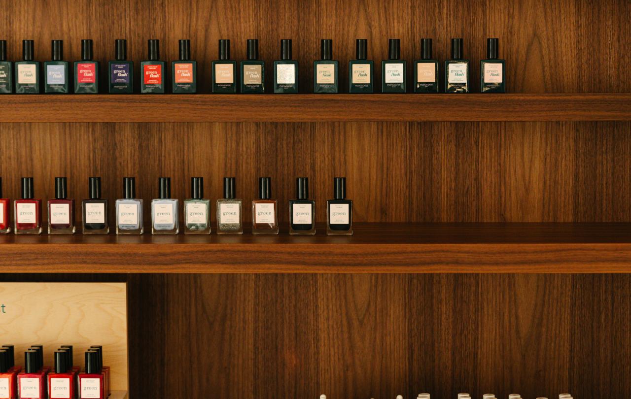 Rows of colorful nail polish bottles displayed on dark wooden shelves, with additional bottles arranged on countertop stands labeled “manucurist Paris.”