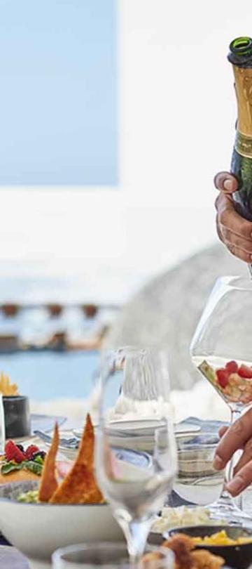A close up of a man preparing to pour wine into a glass that already contains pieces of fruit.