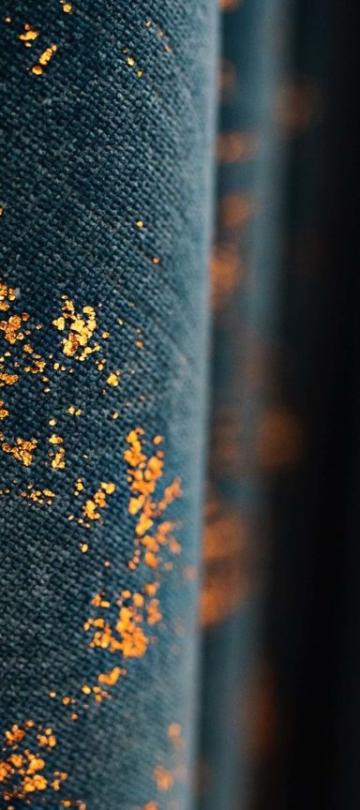 A close up of dark blue curtains with gold foiling in a scattered pattern across the fabric surface.