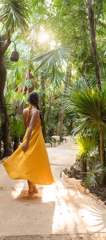 woman in yellow dress walks through jungle