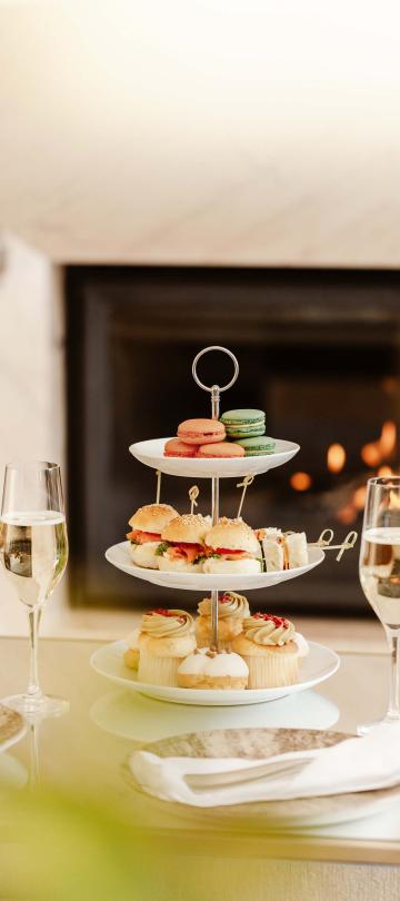 tiered dessert with cupcakes and macarons sits on table beside glasses of wine