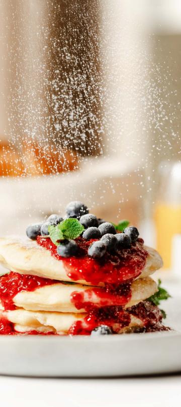 powdered sugar falling onto stack of pancakes covered in fruit