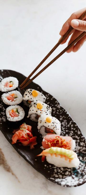 person using chopsticks picks up roll from plate of sushi