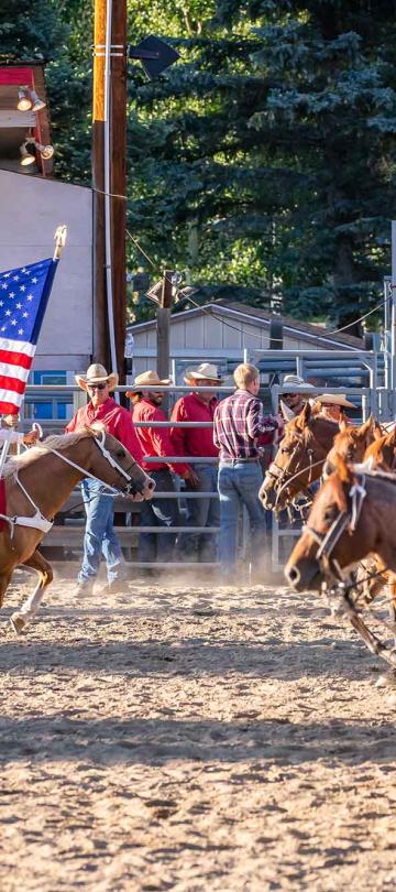 people carrying flags ride horses at rodeo 