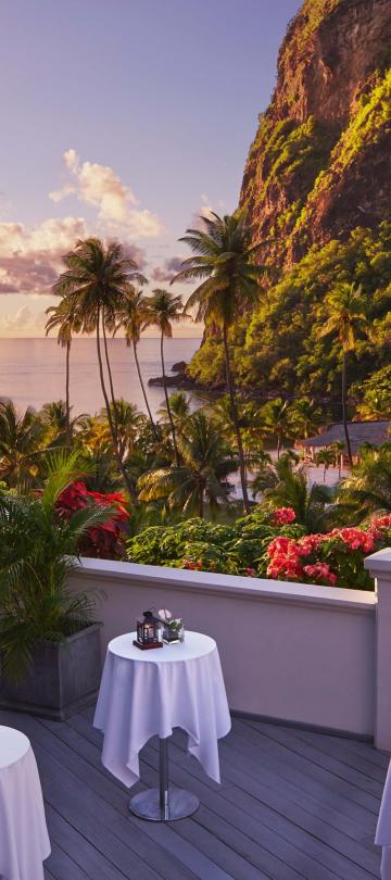 white clothed tables placed on patio overlooking ocean, beach, and mountains