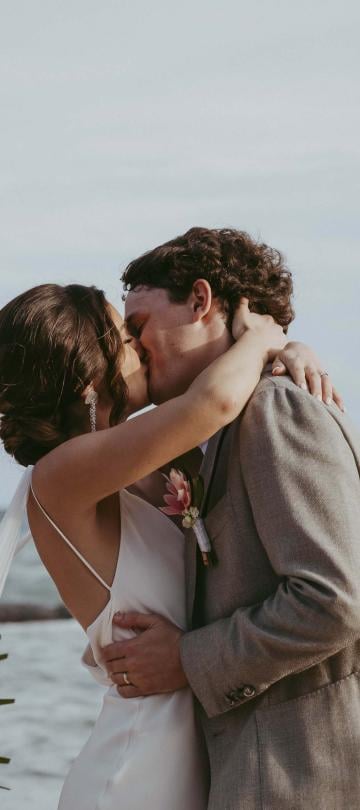 a bride and groom kissing on the beach