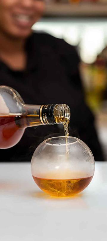 Bartender pouring rum into a spherical glass