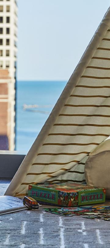 A triangular teepee-style children's pop-tent set up in a hotel room looking out on the Chicago skyline