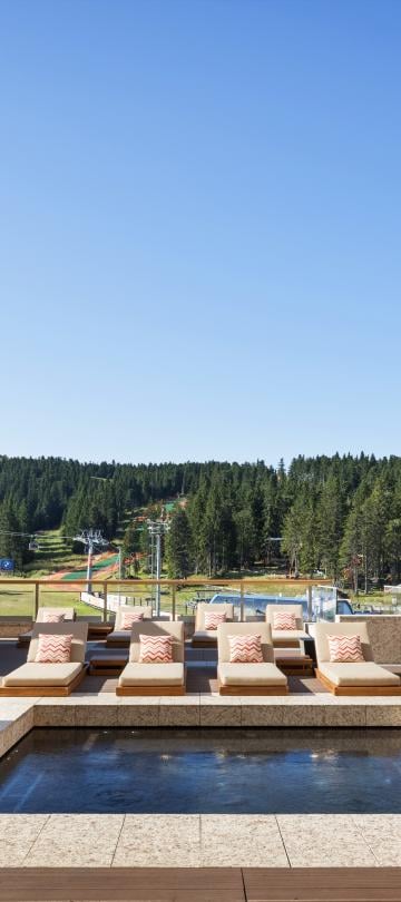 A whirlpool surrounded by pool cabanas, with rolling green tree-topped hills in the background