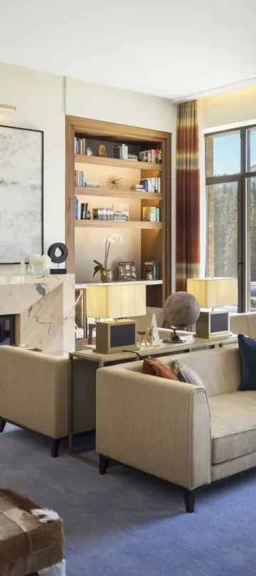 The Library, an airy lounge at Viceroy Kopaonik Serbia, with ample comfortable seating and several wall-to-ceiling bookshelves and a view of the mountain