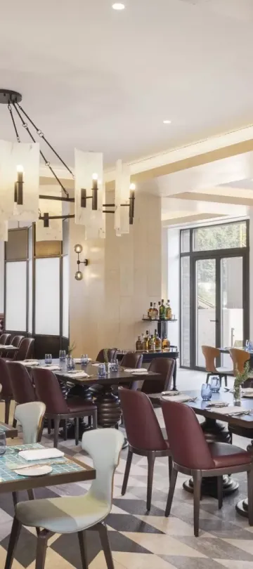 The Mountain Kitchen at Viceroy Kopaonik Serbia, a large bright room with a long row of benches and tables with high-back chairs, under a large chandelier