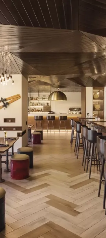The dining room of Pique Ski Bar, with a long bar, several tables and ski paraphenalia decorating the ceiling