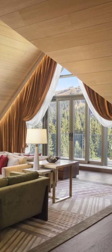 The living space of a penthouse suiter with 2 couches, a large dining table, a floor to ceiling bookshelf and unique drop ceilings A washroom with a large double sink vanity and a soaker tub in a penthouse suite at Viceroy Kopaonik Serbia