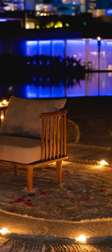 A table set up for two people on the beach with lights in the sand, rose pedals, and a bottle of chilled champagne at Los Cabos 