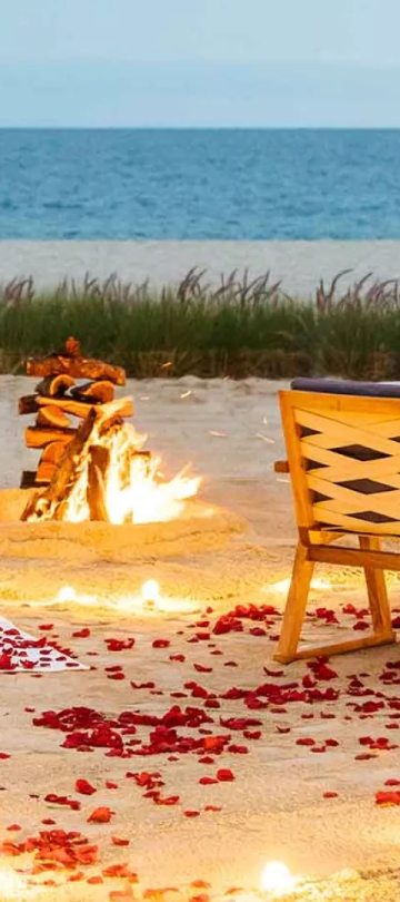 A table with wine and food setup on the beach with a fire and rose pedals laid on the ground at Viceroy Los Cabos