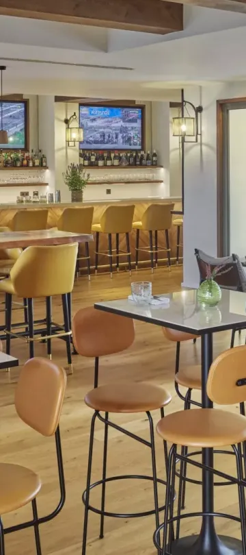 The Casa e Fora dining room at Ombria Algarve, with high four-top tables and a long bar section with wall-mounted televisions