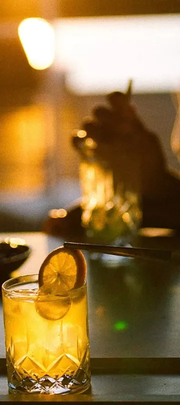 Patrons around a table at Salpico Pool Bar enjoy a bright orange drink with an orange garnish, at dusk