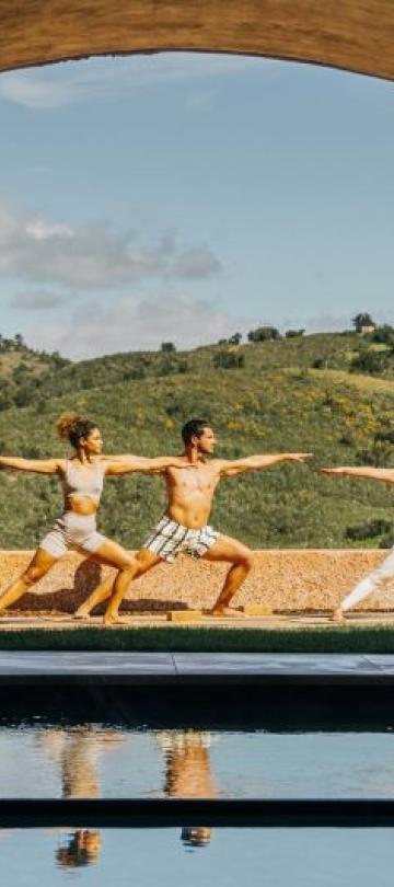 Three people doing yoga in a spa courtyard at Viceroy Ombria Algarve, with rolling hills in the background