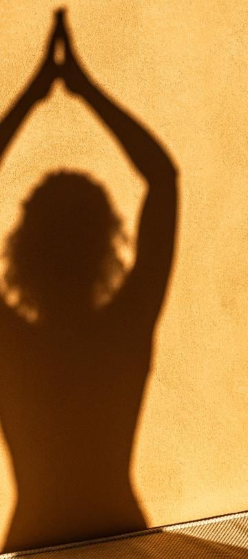 The shadow of a person doing a yoga pose on a stone wall