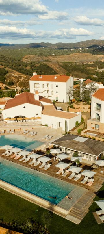Aerial view of the Viceroy Ombria Algarve, with a pool surrounded by white villas with roofs in a lush green hilly landscape