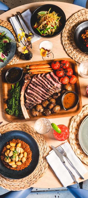 A tomahawk steak, sliced, with accompanying dishes