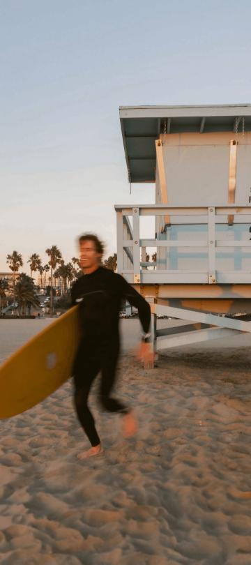 2 men running with surfboards on the beach at Viceroy Santa Monica