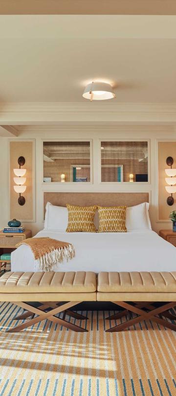A beautiful large room at Viceroy Santa Monaca with a large bed, two lounge chairs, and a surf board on the wall 