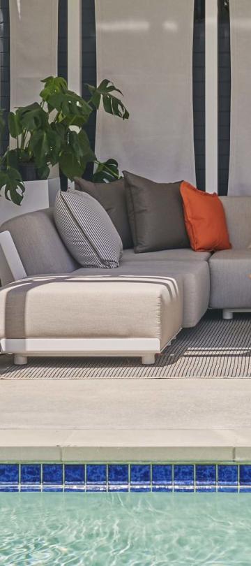 A small dog hanging out on a couch in a poolside cabana