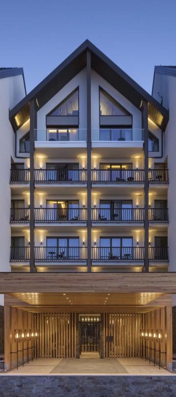 The exterior of Viceroy Kopaonik Serbia at dusk, a large metal and glass building with a wood canopy entryway