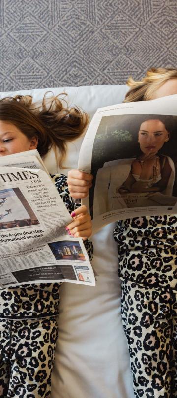 Two kids reading newspapers on a bed