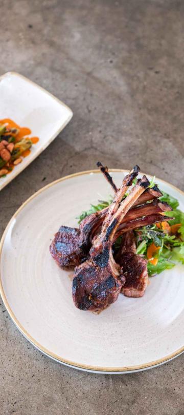 A plate of steak next to a plate of asparagus. A woman is holding a glass of red wine.