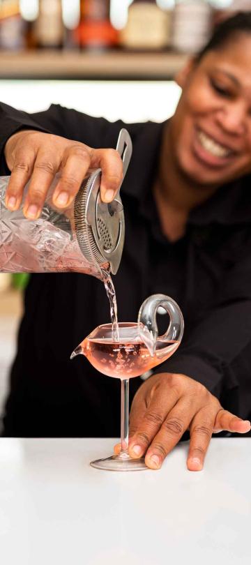 A bartender smiles while pouring a shaken cocktail at Saltwood Restaurant