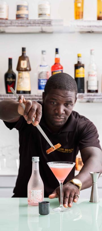 A bartender places the finishing garnish on a pink cocktail at The Cane Bar