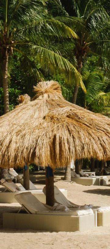 Beach recliners on Sugar Beach at the base of a mountain, each with thatched roof canopies