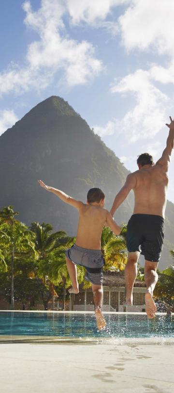 A father and son jumping into the pool at Viceroy Sugar Beach with beautiful mountains ion the foreground