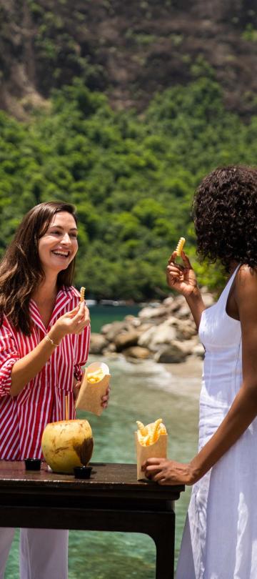 Two women eating and drinking with the beach in the background