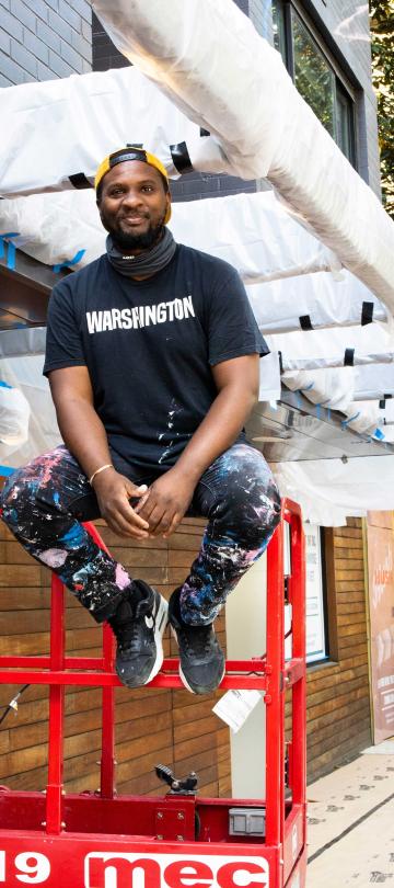 An artist from No Kings Collective sits on scaffolding outside Viceroy Washington DC