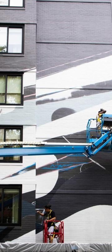 An artist uses a crane to paint graffiti on a high wall at Viceroy Washington DC